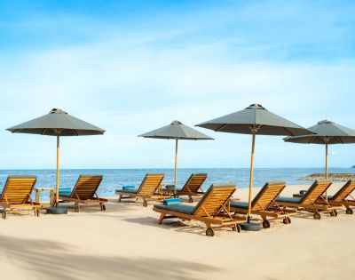 Sandy beach with wooden lounge chairs and grey umbrellas facing a calm blue ocean under a clear sky; a serene and inviting atmosphere.