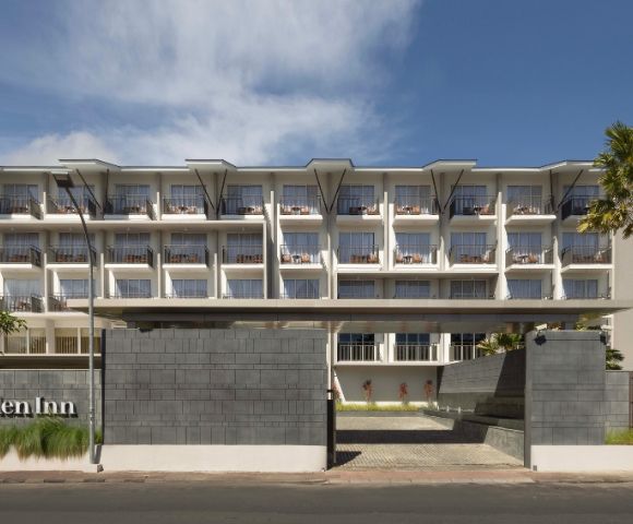 Four-story Hilton Garden Inn hotel exterior with modern design, large windows, and a welcoming atmosphere under a clear blue sky.