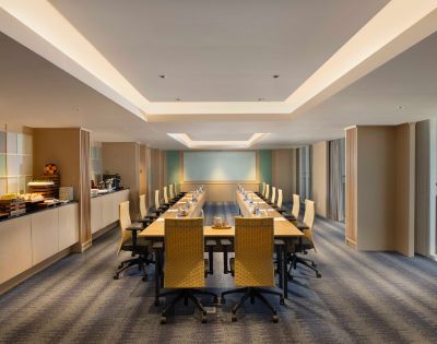 A spacious, modern conference room with a long wooden table, beige chairs, and soft lighting. Walls feature subtle artwork, creating a professional atmosphere.