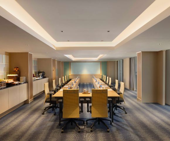 A spacious, modern conference room with a long wooden table, beige chairs, and soft lighting. Walls feature subtle artwork, creating a professional atmosphere.