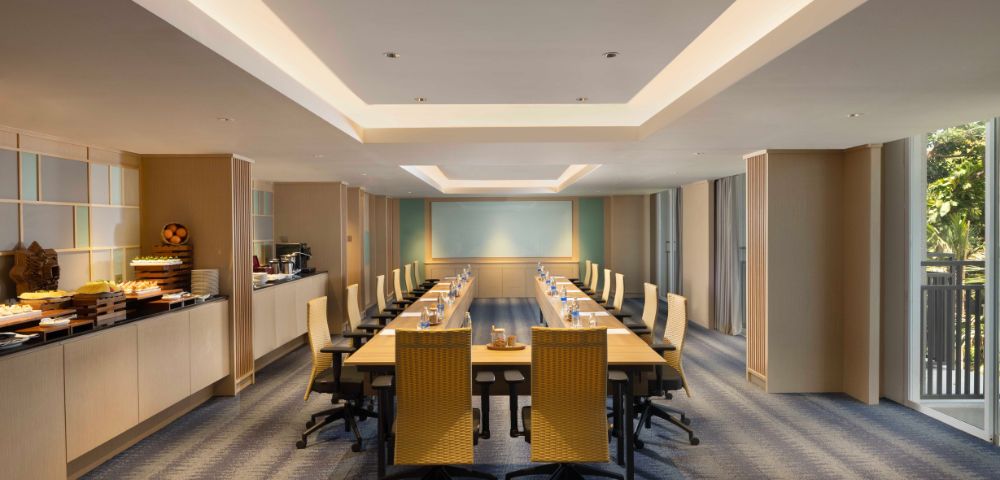A spacious, modern conference room with a long wooden table, beige chairs, and soft lighting. Walls feature subtle artwork, creating a professional atmosphere.