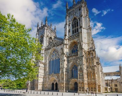 Gothic cathedral under a vibrant blue sky, adorned with intricate spires and arched windows. A lush green tree adds contrast, conveying serenity and grandeur.
