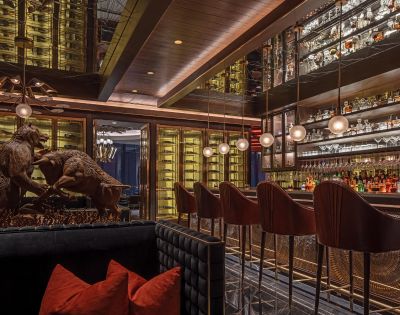 Sophisticated bar interior with plush seating, a statue of fighting animals, and a well-stocked, illuminated bar. Warm lighting creates an elegant ambiance.