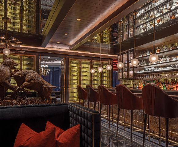 Sophisticated bar interior with plush seating, a statue of fighting animals, and a well-stocked, illuminated bar. Warm lighting creates an elegant ambiance.