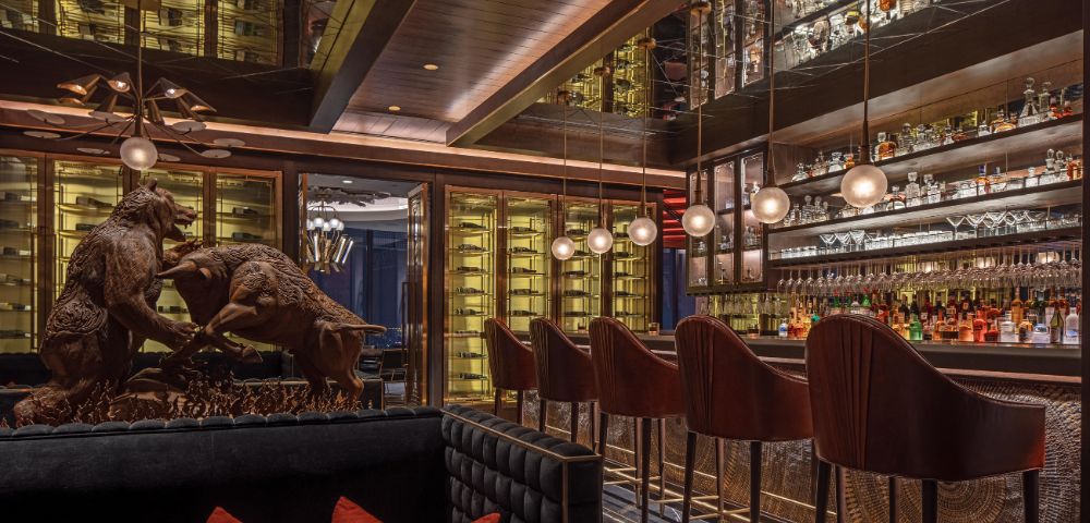 Sophisticated bar interior with plush seating, a statue of fighting animals, and a well-stocked, illuminated bar. Warm lighting creates an elegant ambiance.
