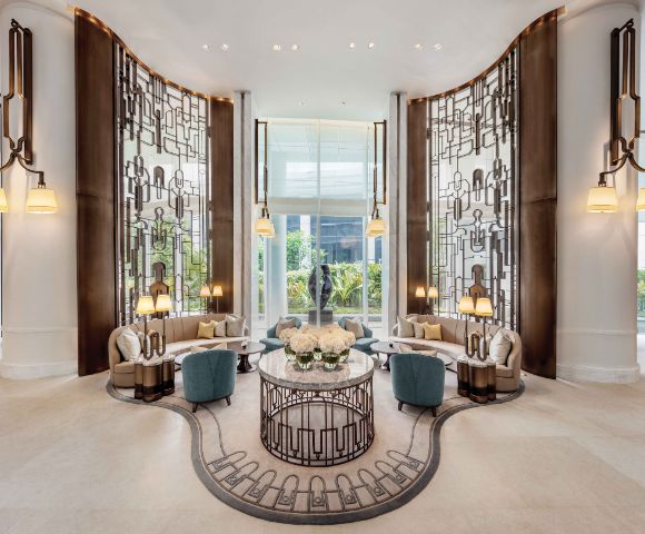 Luxurious hotel lobby with ornate metal screens, elegant seating, and warm lighting. Central floral arrangement on a round table exudes sophistication.