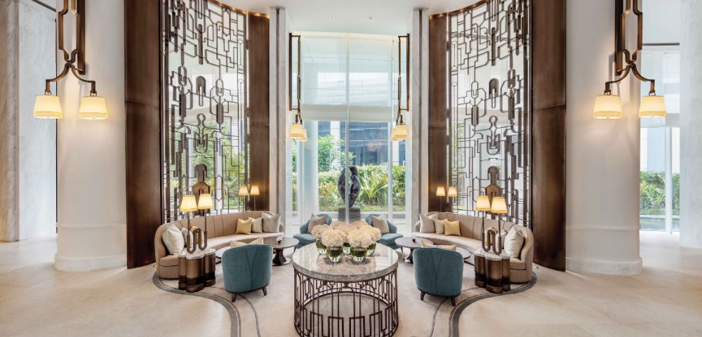 Luxurious hotel lobby with ornate metal screens, elegant seating, and warm lighting. Central floral arrangement on a round table exudes sophistication.