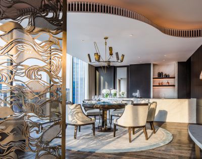 Elegant dining room with a modern chandelier, round table surrounded by white chairs, decorative screen, and a sophisticated ambient reflecting luxury.