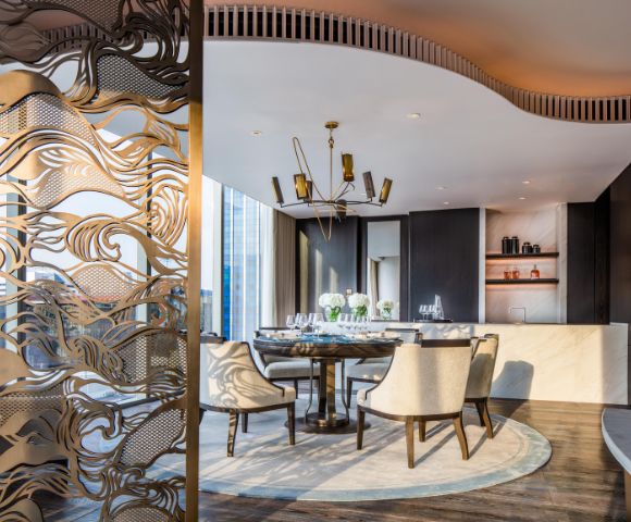 Elegant dining room with a modern chandelier, round table surrounded by white chairs, decorative screen, and a sophisticated ambient reflecting luxury.