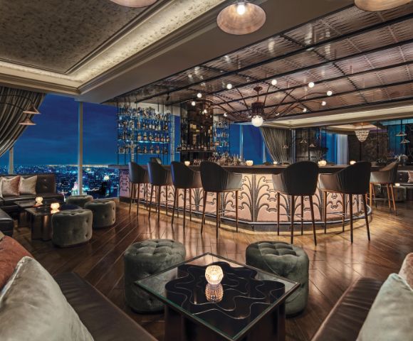 Luxurious rooftop bar with elegant decor, featuring plush seating and a curved bar, overlooking a cityscape at night. Warm, inviting ambiance.