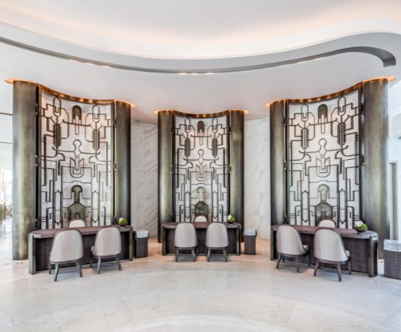 Elegant hotel lobby with modern decor features three artistic, geometric wall panels. Curved desks and chairs add sophistication, while lighting sets a calming tone.