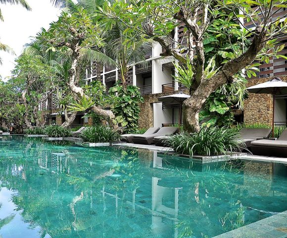 Luxurious resort pool surrounded by lush greenery and elegant sun loungers. Tall palms and vibrant plants create a serene, tropical ambiance.