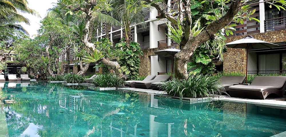 Luxurious resort pool surrounded by lush greenery and elegant sun loungers. Tall palms and vibrant plants create a serene, tropical ambiance.