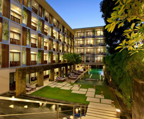 Modern hotel courtyard at dusk with a central pool, surrounded by multi-story buildings. Lounge chairs line the poolside, creating a serene, inviting atmosphere.