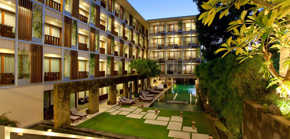 Modern hotel courtyard at dusk with a central pool, surrounded by multi-story buildings. Lounge chairs line the poolside, creating a serene, inviting atmosphere.