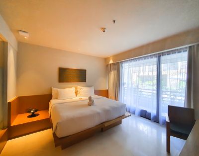 A minimalist hotel room with a king-sized bed adorned with white linens and a towel swan. Soft lighting, large window with sheer curtains, and a serene ambiance.