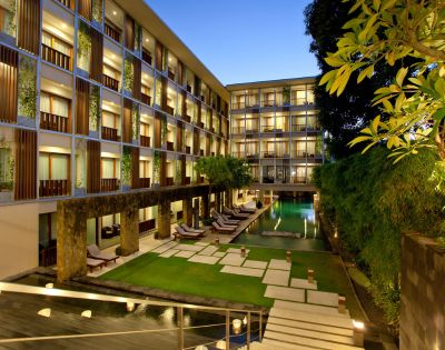Modern hotel courtyard at dusk with a central pool, surrounded by multi-story buildings. Lounge chairs line the poolside, creating a serene, inviting atmosphere.