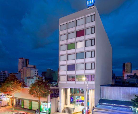 Modern hotel building at dusk, with a colorful window pattern and vibrant street below. The sky is dark, setting a calm urban atmosphere.
