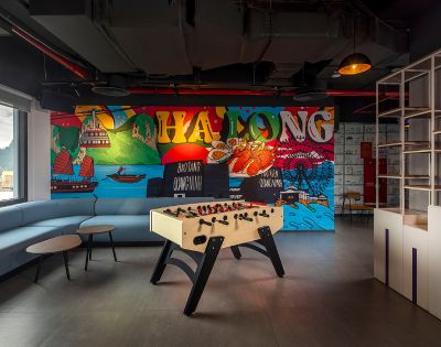 Modern lounge with a foosball table and colorful mural of Ha Long Bay. A curved sofa and round tables add a relaxed, playful atmosphere.