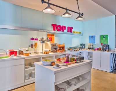 Bright hotel breakfast buffet with various food options, including cereals, bread, and toppings. Modern decor, inviting atmosphere, and vibrant 