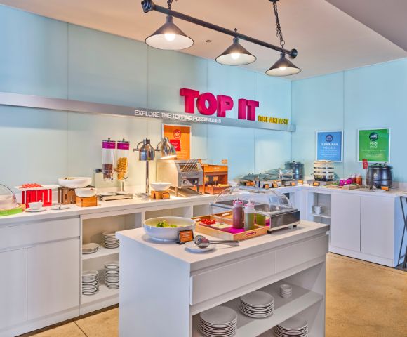 Bright hotel breakfast buffet with various food options, including cereals, bread, and toppings. Modern decor, inviting atmosphere, and vibrant 