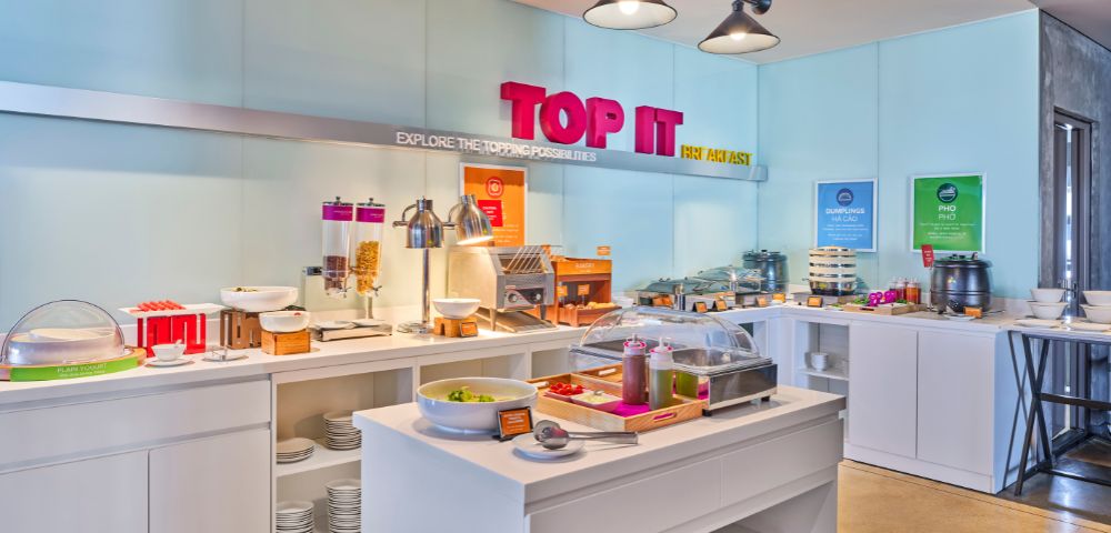 Bright hotel breakfast buffet with various food options, including cereals, bread, and toppings. Modern decor, inviting atmosphere, and vibrant 