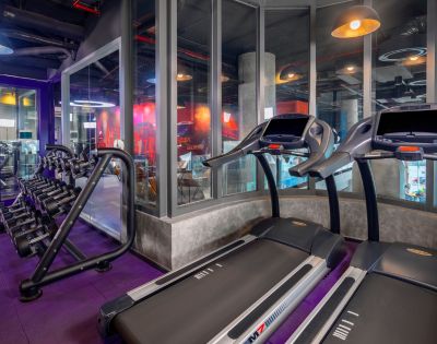 A modern gym interior featuring rows of treadmills and elliptical machines. Bright lighting and mirrored walls create an energetic and welcoming atmosphere.