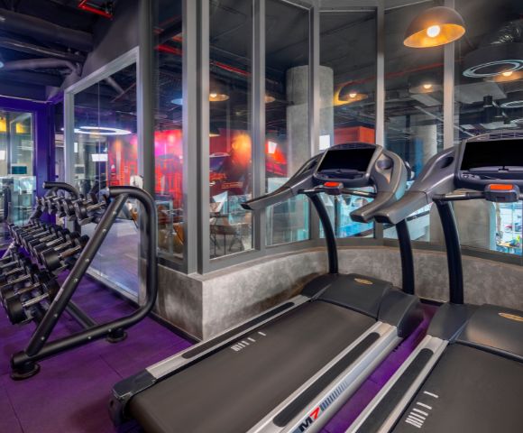 A modern gym interior featuring rows of treadmills and elliptical machines. Bright lighting and mirrored walls create an energetic and welcoming atmosphere.