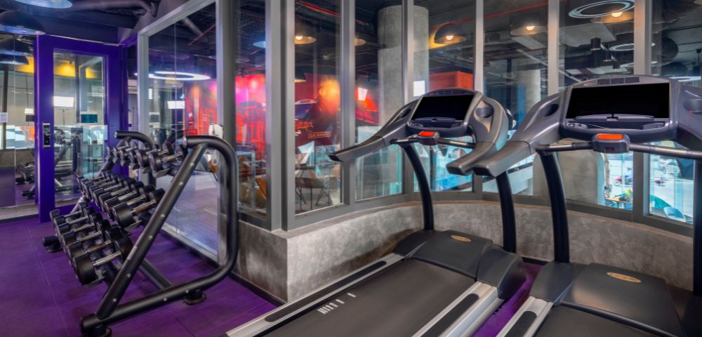 A modern gym interior featuring rows of treadmills and elliptical machines. Bright lighting and mirrored walls create an energetic and welcoming atmosphere.