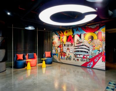 A modern room with bright, artistic Hanoi-themed graffiti on the wall. Two colorful chairs and small tables sit beneath a circular ceiling light.