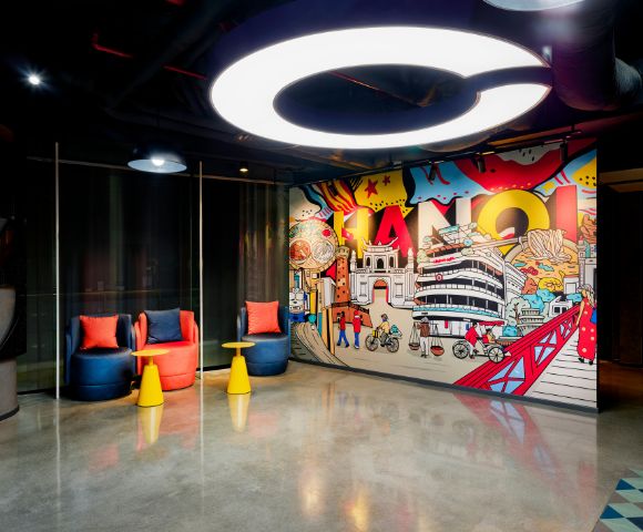 A modern room with bright, artistic Hanoi-themed graffiti on the wall. Two colorful chairs and small tables sit beneath a circular ceiling light.