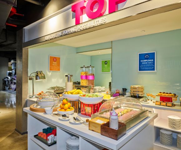 Spacious buffet area with a variety of breakfast items, including fruits, cereals, and drinks. Bright lighting creates a welcoming atmosphere.