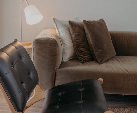 A cozy living room features a brown velvet sofa with plush cushions, a modern black leather chair, and a soft-lit floor lamp, offering a warm and inviting ambiance.
