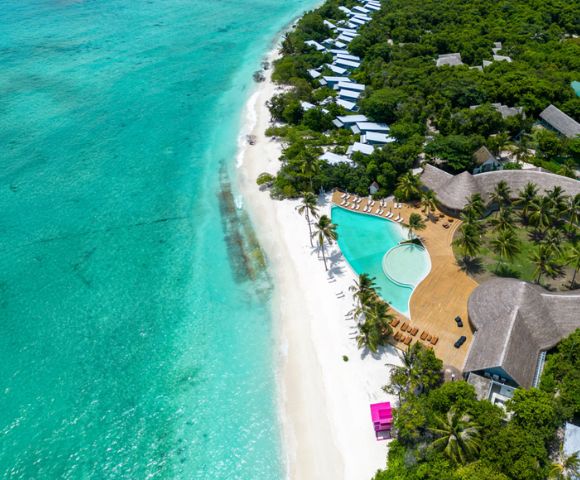 Aerial view of a tropical beach with turquoise waters, white sand, palm trees, luxury villas, and a pool. Lush greenery surrounds the tranquil setting.