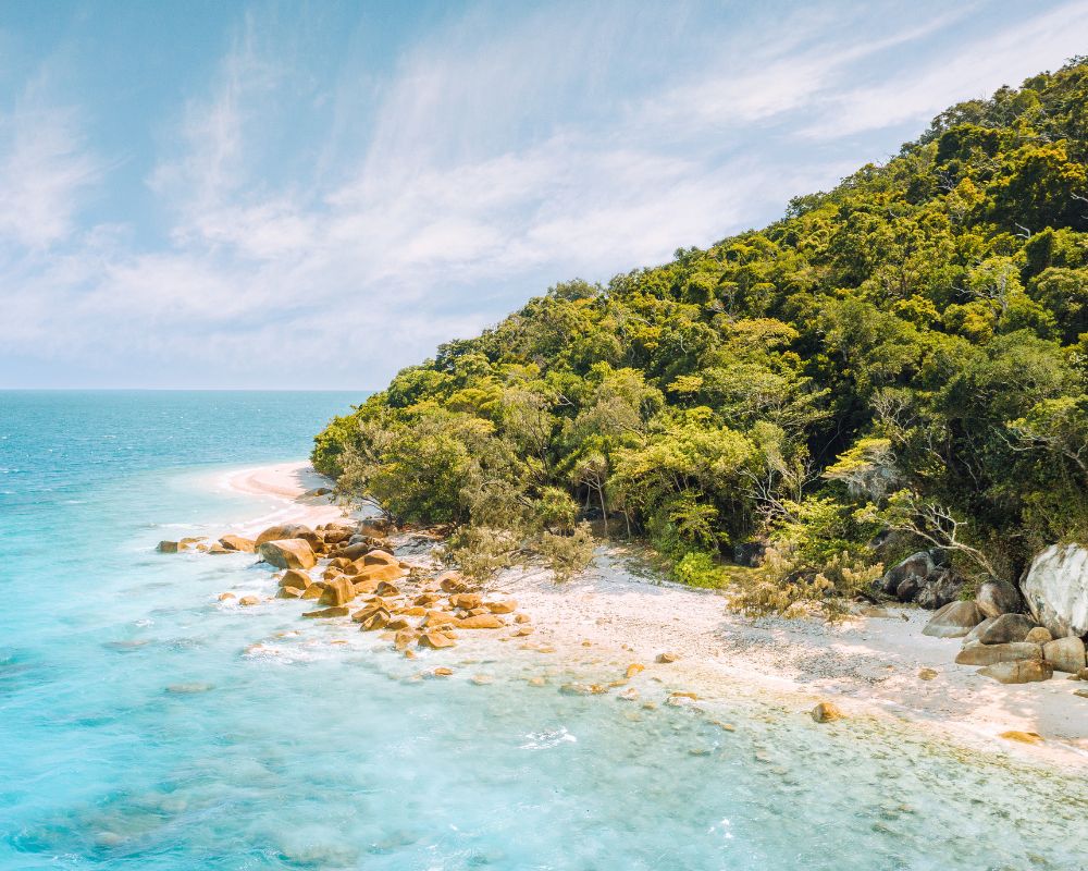 A serene tropical beach with clear turquoise water, rocky shorelines, and lush green forest under a clear blue sky, conveying tranquility and beauty.