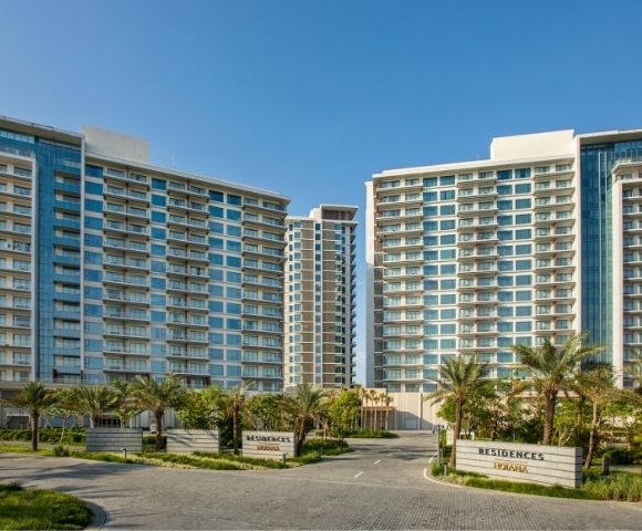 Modern residential towers against a clear blue sky, with palm trees and neatly manicured lawns in the foreground, conveying a serene, upscale atmosphere.