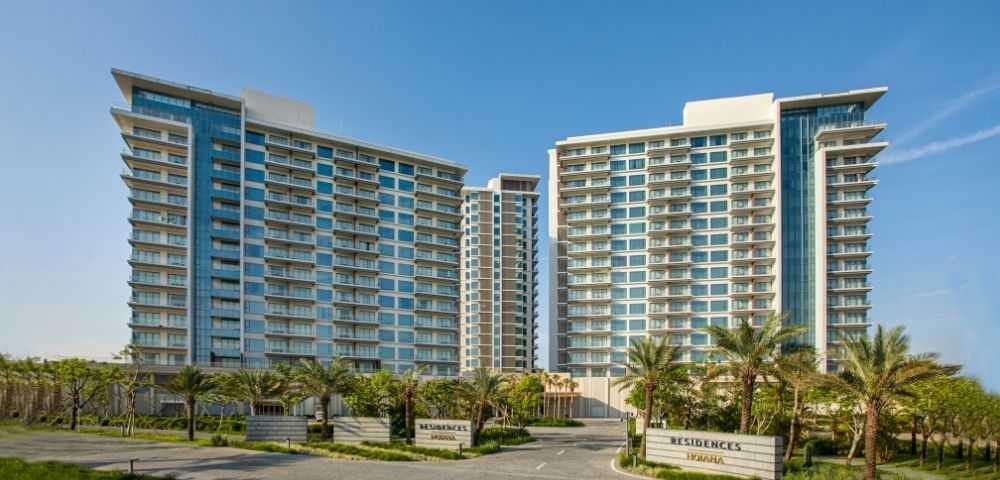 Modern residential towers against a clear blue sky, with palm trees and neatly manicured lawns in the foreground, conveying a serene, upscale atmosphere.