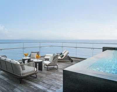 Rooftop patio with wicker furniture and a lounge chair, overlooking the ocean. Nearby, a modern infinity pool adds to the serene, luxurious ambiance.