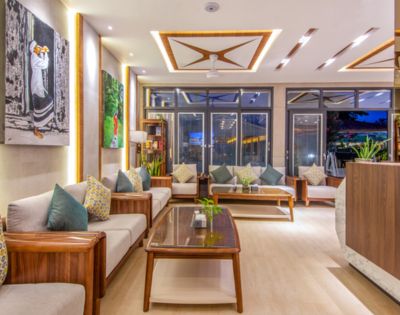 A modern living room with elegant wooden furniture, plush cushions, and vibrant artwork. Large windows and soft lighting create a cozy, inviting ambiance.