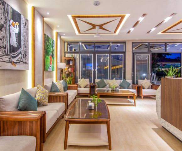 A modern living room with elegant wooden furniture, plush cushions, and vibrant artwork. Large windows and soft lighting create a cozy, inviting ambiance.