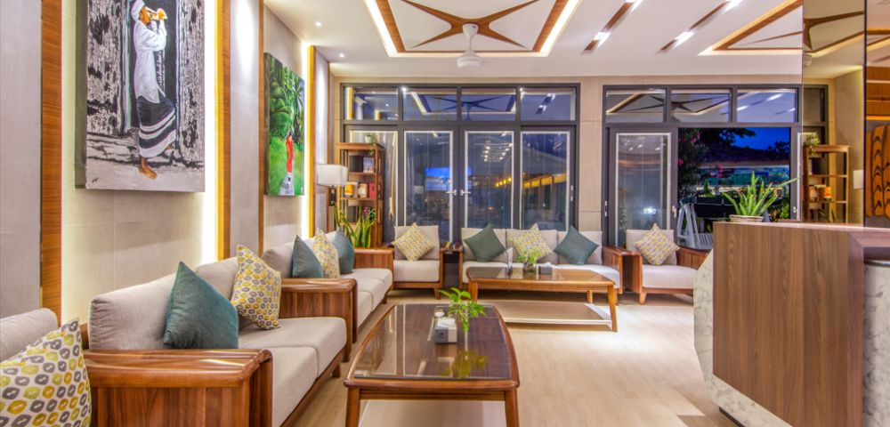 A modern living room with elegant wooden furniture, plush cushions, and vibrant artwork. Large windows and soft lighting create a cozy, inviting ambiance.