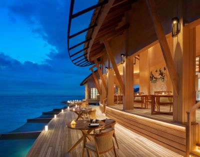 Wooden deck at a luxurious beachside resort at twilight, with soft lighting, elegant outdoor seating, and ocean view, creating a serene, inviting atmosphere.