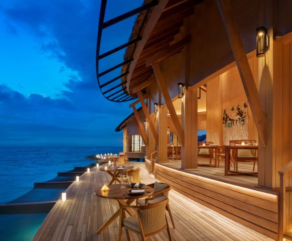 Wooden deck at a luxurious beachside resort at twilight, with soft lighting, elegant outdoor seating, and ocean view, creating a serene, inviting atmosphere.