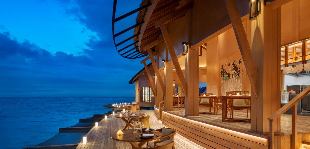 Wooden deck at a luxurious beachside resort at twilight, with soft lighting, elegant outdoor seating, and ocean view, creating a serene, inviting atmosphere.