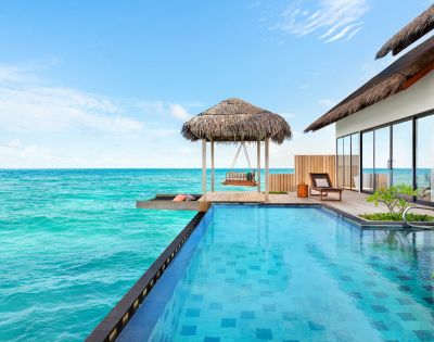 Luxurious oceanfront villa with an infinity pool, thatched-roof gazebo, and sun loungers. The tranquil turquoise sea and clear blue sky create a serene atmosphere.