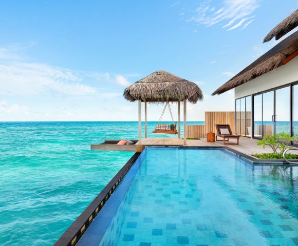 Luxurious oceanfront villa with an infinity pool, thatched-roof gazebo, and sun loungers. The tranquil turquoise sea and clear blue sky create a serene atmosphere.