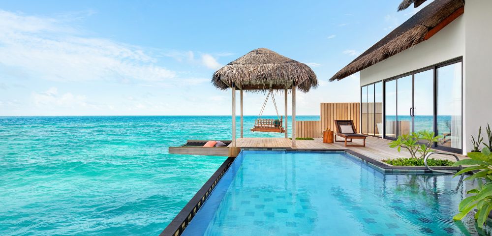 Luxurious oceanfront villa with an infinity pool, thatched-roof gazebo, and sun loungers. The tranquil turquoise sea and clear blue sky create a serene atmosphere.