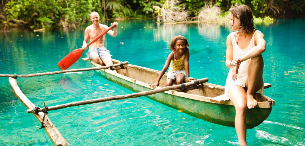 A family paddles a canoe together in clear blue water, enjoying a sunny day outdoors.