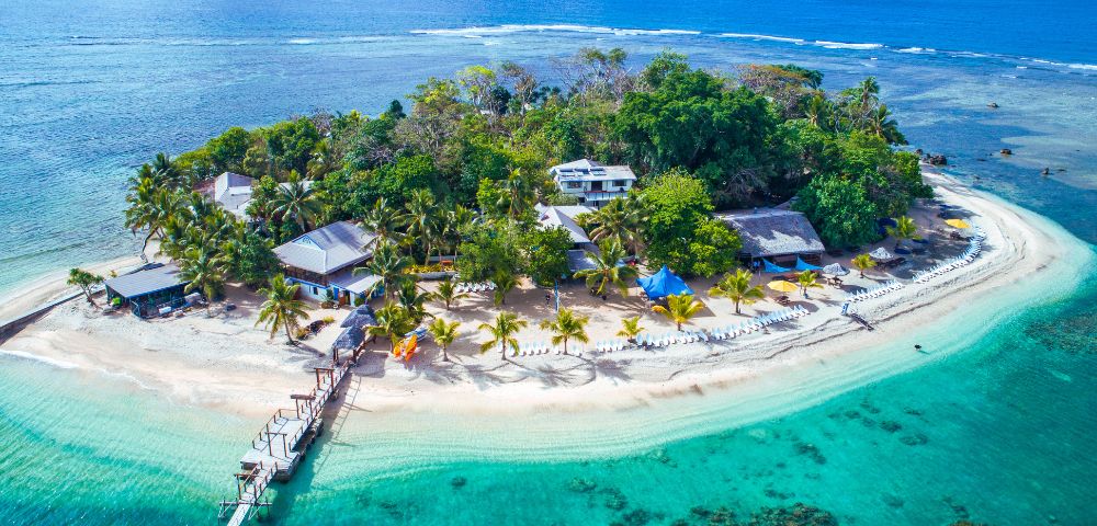 A resort sits on a serene island surrounded by calm waters and lush greenery.