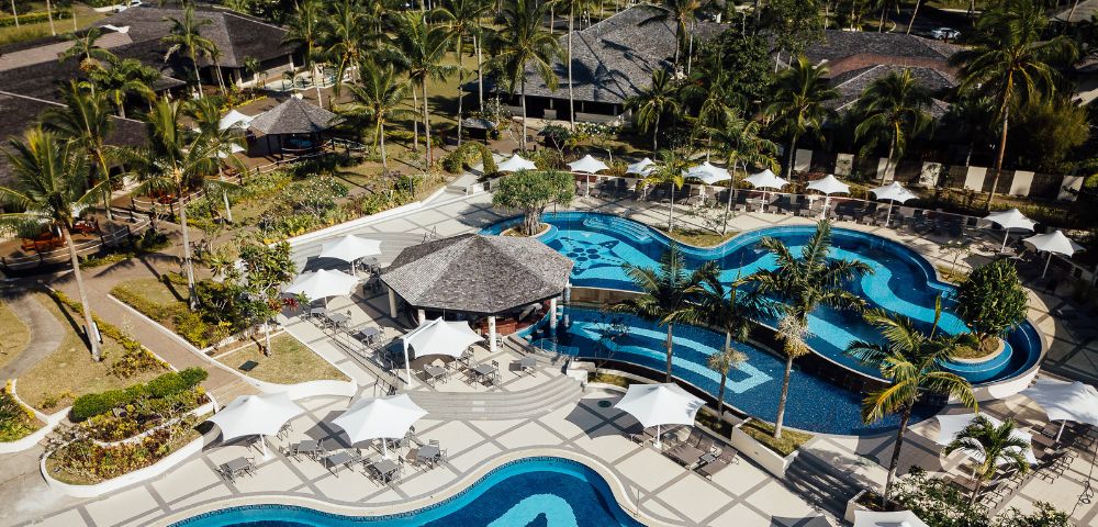 A serene view of the resort pool surrounded by lounge chairs and palm trees under a clear blue sky.